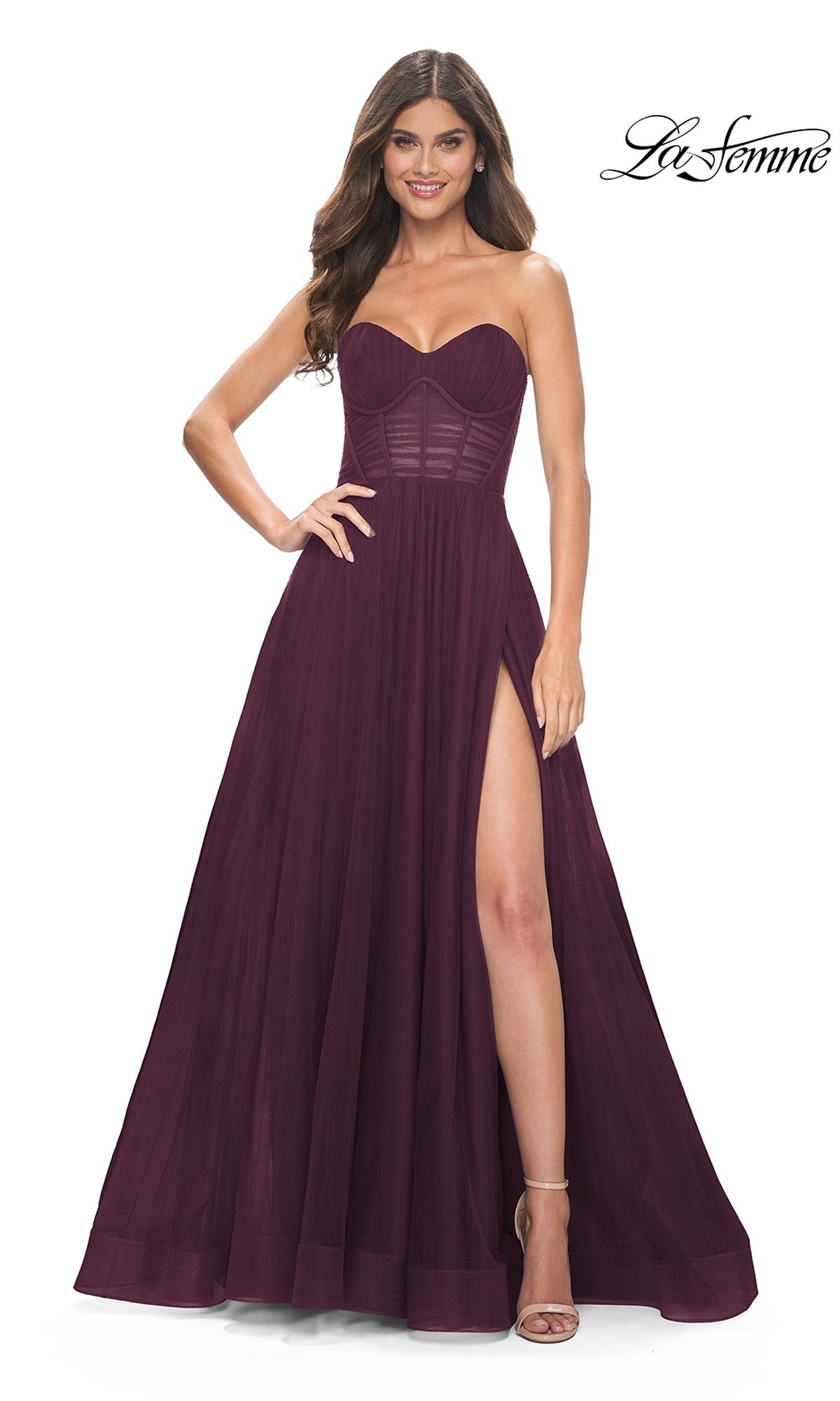 A woman in the La Femme Strapless Long A-Line Prom Dress 31971, a dark burgundy gown with a corset bodice and high slit, stands and smiles. The La Femme logo appears in the top right corner.